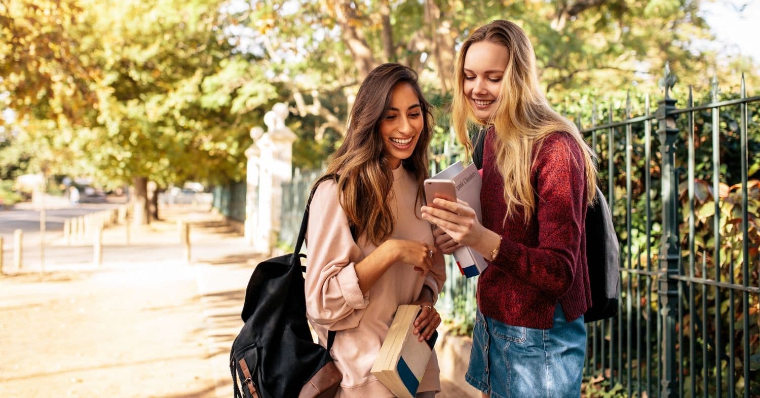 Two college students on campus, smiling while scrolling on a phone