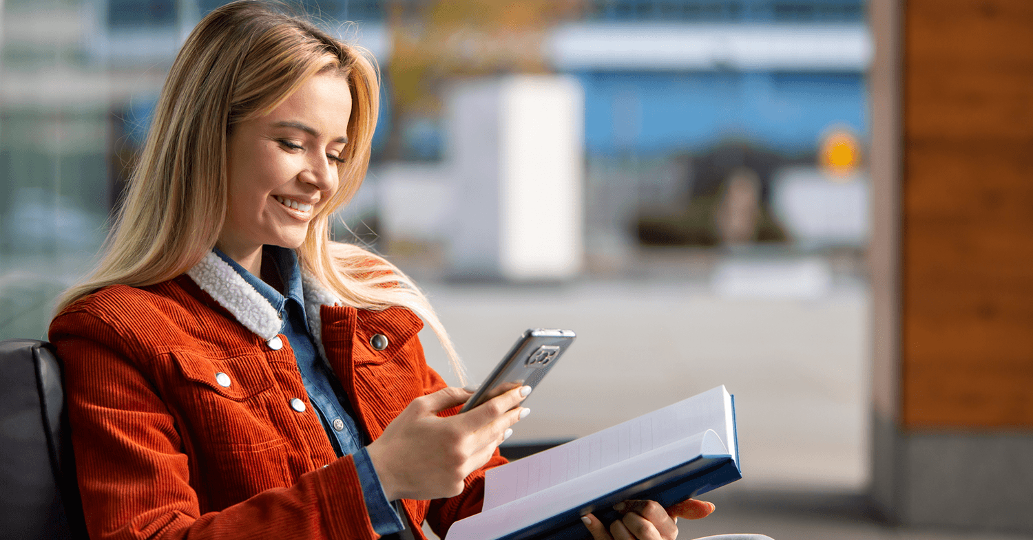 University student browsing her phone and studying a book